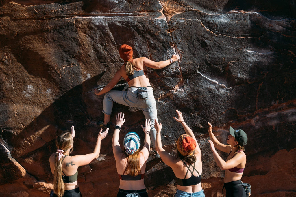Woman climber bouldering in Moab Utah, supported by several female spotters all wearing Têra Kaia TOURA basewear top outdoor sports bras with strappy criss cross racerbacks